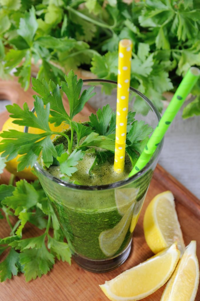 Parsley juice with yellow and green straw on a wooden table with lemons